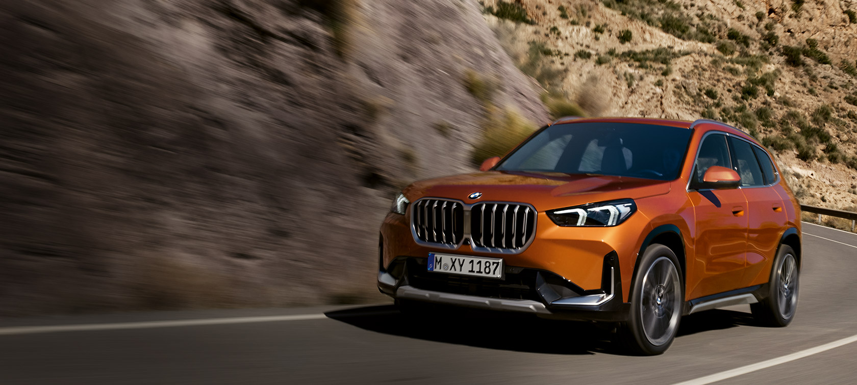 BMW X1 U11 xLine Utah orange metallic three quarter front view driving on country road